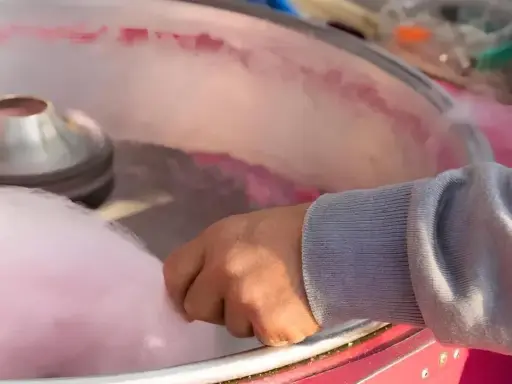 Main d'une personne récoltant du sucre filé rose, étape clé pour savoir comment faire du sucre à barbe à papa.