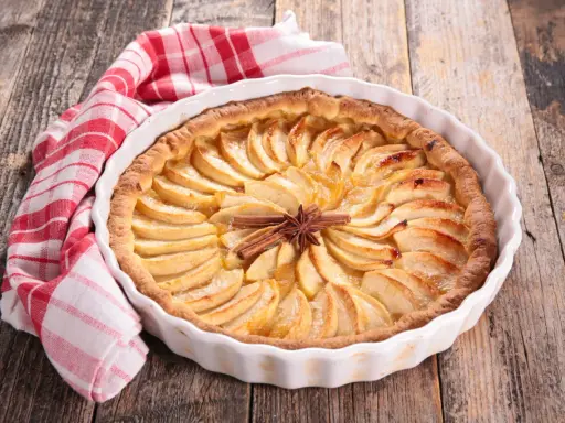 Tarte aux pommes dorée, décorée de bâtons de cannelle et d'anis étoilé. Une serviette à carreaux rouges et blancs est posée à côté. Idéale pour la conservation.