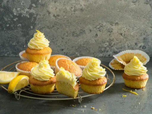 Plusieurs cupcakes citron avec un glaçage jaune vif, certains décorés de zestes. Des quartiers de citron frais sont posés à côté.