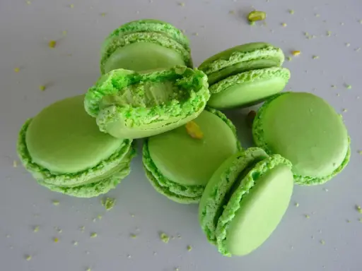 Macarons verts vifs, certains ouverts révélant une garniture crémeuse. Parfaits pour une recette ganache pistache sans chocolat blanc.