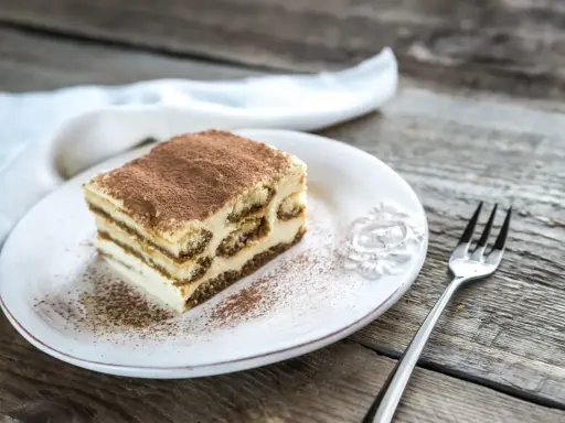 Une part de tiramisu sur une assiette blanche, saupoudrée de cacao. Combien de temps au frigo pour ce délice ?