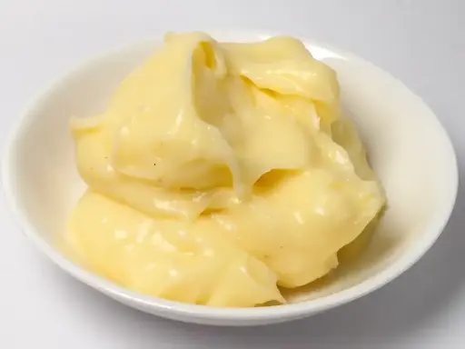 Crème pâtissière onctueuse, légèrement granuleuse, dans un bol blanc. Des points noirs de vanille parsèment la texture crémeuse.