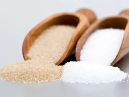 Deux cuillères en bois contiennent différents types de sucre en pâtisserie : du sucre blanc et du sucre roux.