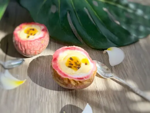 Deux moitiés de fruit de la passion garnies d'une crème jaune et de graines noires, sur une table en bois, avec une feuille tropicale et des pétales de fleurs.