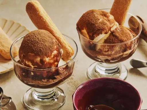 Deux coupes de glace tiramisu, saupoudrées de cacao, avec des biscuits à la cuillère. Un délice glacé à savourer.