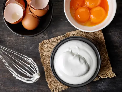 Préparation d'une meringue : blancs en neige, jaunes d'œufs, coquilles et fouet sur fond de bois sombre.