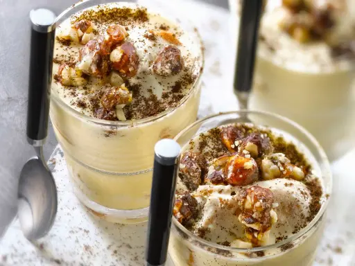Deux verrines de tiramisu noisette, garnies de noisettes caramélisées et saupoudrées de cacao.