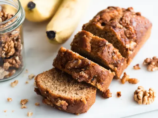 Tranches de délicieux dessert banane et noix, avec des bananes et des noix à proximité.