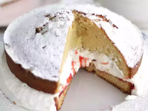 Un délicieux victoria cake, saupoudré de sucre glace, révèle sa garniture crémeuse et sa confiture de fruits rouges.