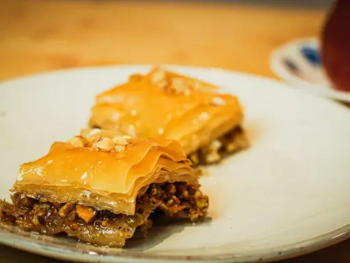 Deux parts de baklava, garnies de noix, sur une assiette. Une recette de baklava qui fait saliver.