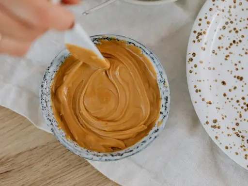 Une spatule prélève une portion de crème d'amandes légère dans un bol. Une assiette tachetée est à côté.