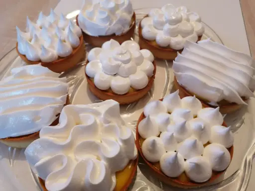 Plusieurs tartelettes garnies de crème citronnée et couronnées de meringue italienne aux formes variées.