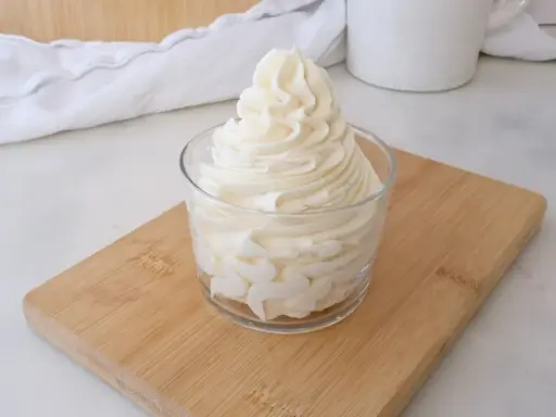 Crème au beurre sucre glace, onctueuse et aérienne, dressée dans un verre sur une planche en bois.
