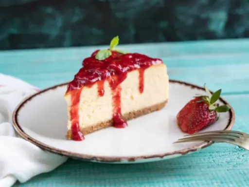 Tranche de cheesecake à la ricotta sans cuisson, nappée de coulis de fraises et décorée d'une feuille de menthe. Une fraise entière et une fourchette complètent la présentation.