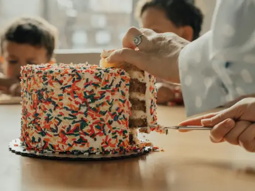 Une main coupe une part d'un gâteau coloré de vermicelles. Apprenez comment couper un layer cake pour un partage parfait.
