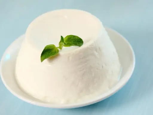 Un dôme de ricotta crémeuse, garni d'une feuille verte, sur une assiette blanche. Découvrez les ricotta bienfaits pour une alimentation saine.