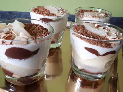 Quatre verrines poire chocolat mascarpone, garnies de copeaux de chocolat et d'amandes effilées, sur un plateau doré.