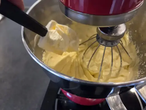 Une spatule ajoute une touche finale à une crème mousseline légère dans un robot pâtissier.