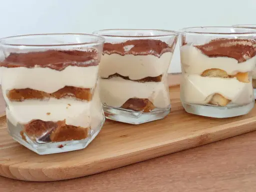 Quatre verrines de tiramisu chantilly mascarpone, superposant biscuits imbibés et crème onctueuse, saupoudrées de cacao.
