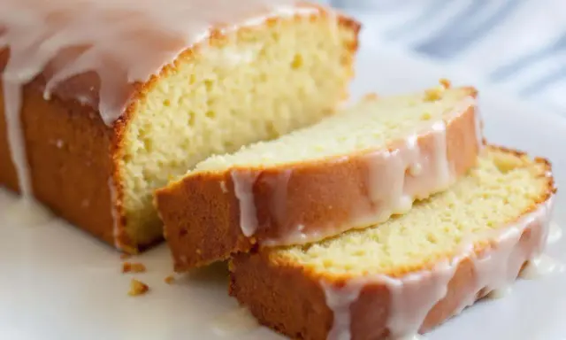Un délicieux gâteau courgette citron, nappé d'un glaçage blanc, est coupé en tranches sur une assiette blanche.