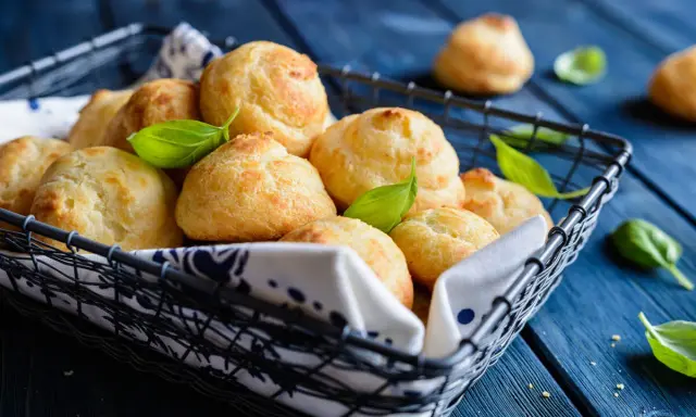 Gougères dorées dans un panier, garnies de feuilles de basilic. Si les vôtres ne gonflent pas, vérifiez la température du four !