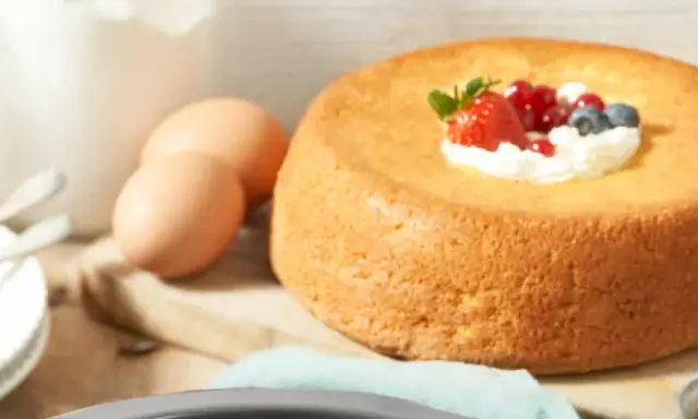 Un savarin traditionnel, doré et moelleux, garni de crème fouettée et de fruits rouges. Des œufs et de la farine sont prêts pour la préparation.