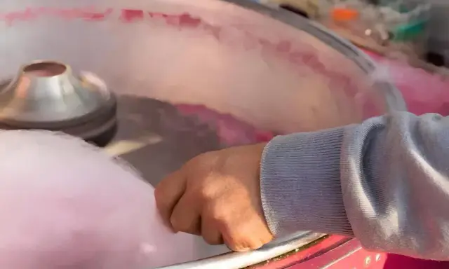 Main d'une personne récoltant du sucre filé rose, étape clé pour savoir comment faire du sucre à barbe à papa.