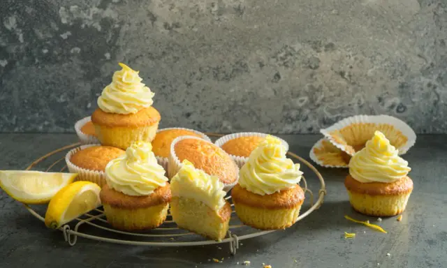 Plusieurs cupcakes citron avec un glaçage jaune vif, certains décorés de zestes. Des quartiers de citron frais sont posés à côté.