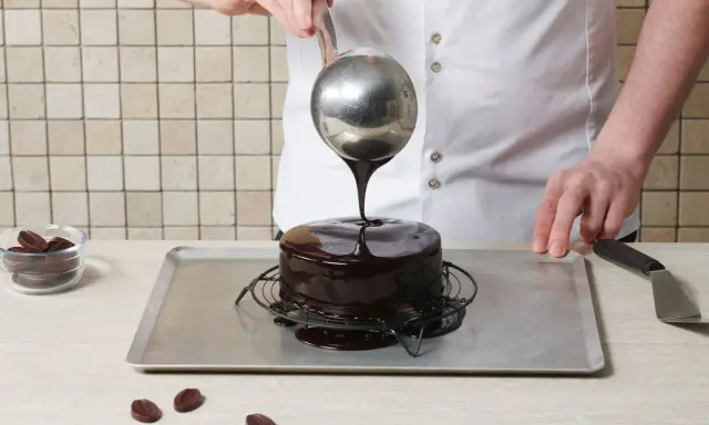 Un chef verse un glaçage au chocolat brillant sur un gâteau rond. Le glaçage sur gâteau froid ou chaud coule parfaitement, créant une finition miroir.