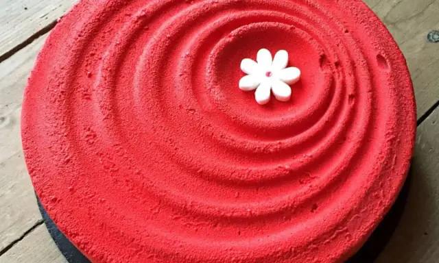 Un tiramisu fraise rhubarbe d'un rouge éclatant, décoré d'une petite fleur blanche en son centre, sur un fond de bois.