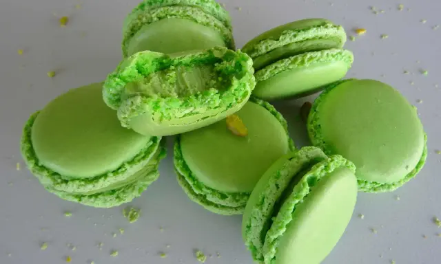 Macarons verts vifs, certains ouverts révélant une garniture crémeuse. Parfaits pour une recette ganache pistache sans chocolat blanc.