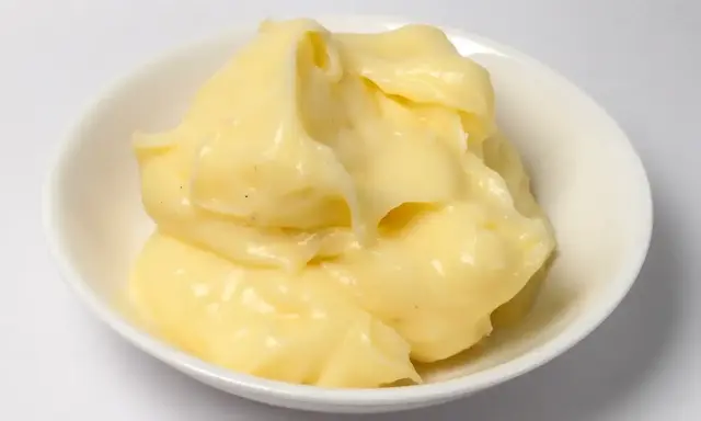 Crème pâtissière onctueuse, légèrement granuleuse, dans un bol blanc. Des points noirs de vanille parsèment la texture crémeuse.