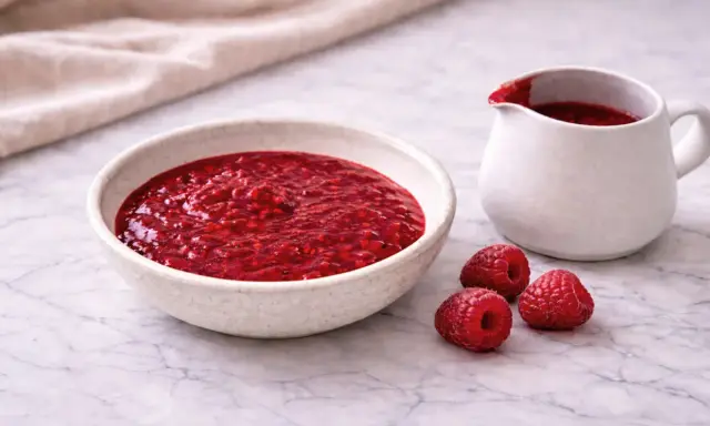 Un bol et un pichet remplis de nappage framboise facile, avec des framboises fraîches à côté.