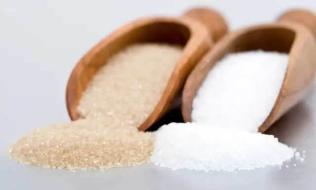 Deux cuillères en bois contiennent différents types de sucre en pâtisserie : du sucre blanc et du sucre roux.