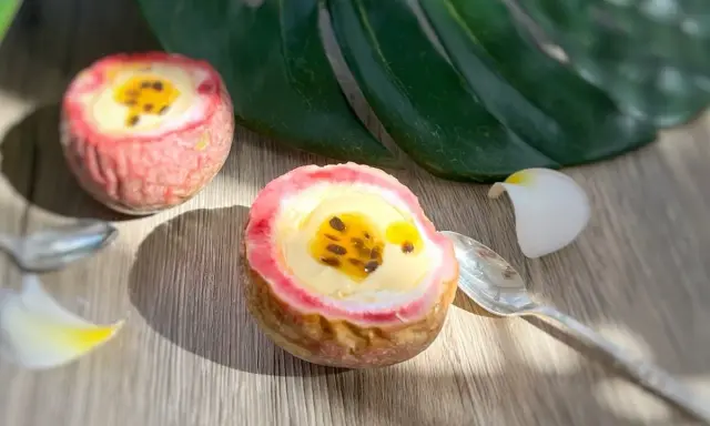 Deux moitiés de fruit de la passion garnies d'une crème jaune et de graines noires, sur une table en bois, avec une feuille tropicale et des pétales de fleurs.
