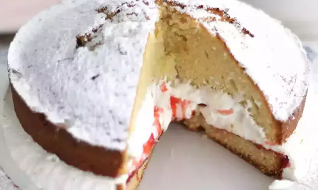 Un délicieux victoria cake, saupoudré de sucre glace, révèle sa garniture crémeuse et sa confiture de fruits rouges.