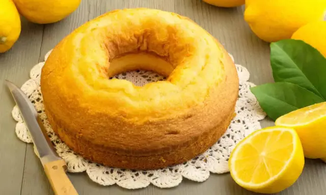 Gâteau moelleux au mascarpone et citron, prêt à être dégusté. Des citrons frais et une touche de verdure complètent la scène.
