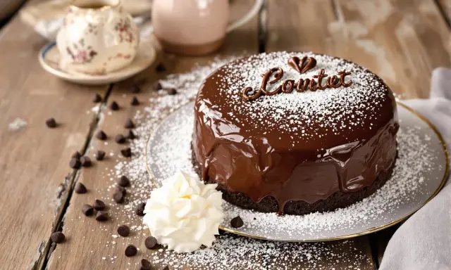 Un délicieux gateau d'anniversaire chocolat, nappé de glaçage brillant et saupoudré de sucre glace. Une touche de crème et des pépites de chocolat complètent cette gourmandise.
