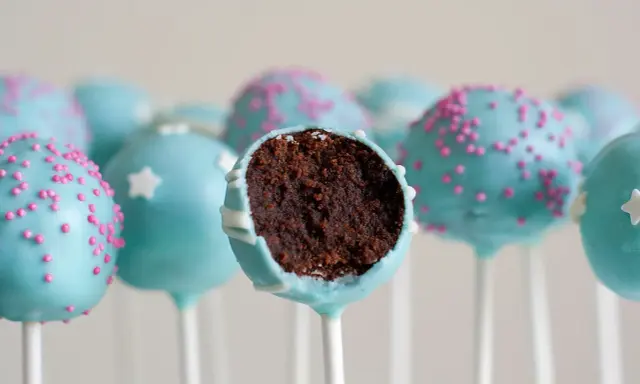 Gourmandes boules de chocolat bleu ciel, décorées de vermicelles roses ou d'étoiles blanches. Une recette facile de cake pop à dévorer !