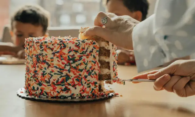 Une main coupe une part d'un gâteau coloré de vermicelles. Apprenez comment couper un layer cake pour un partage parfait.