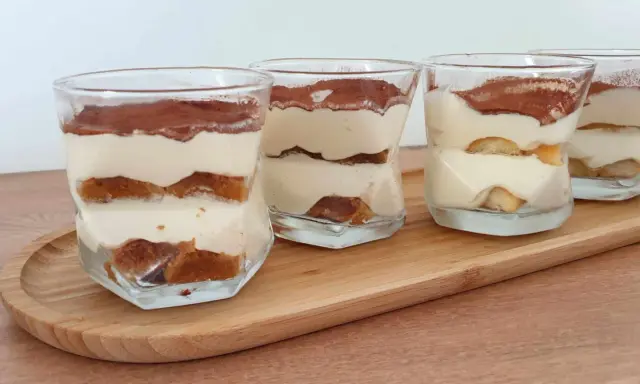 Quatre verrines de tiramisu chantilly mascarpone, superposant biscuits imbibés et crème onctueuse, saupoudrées de cacao.