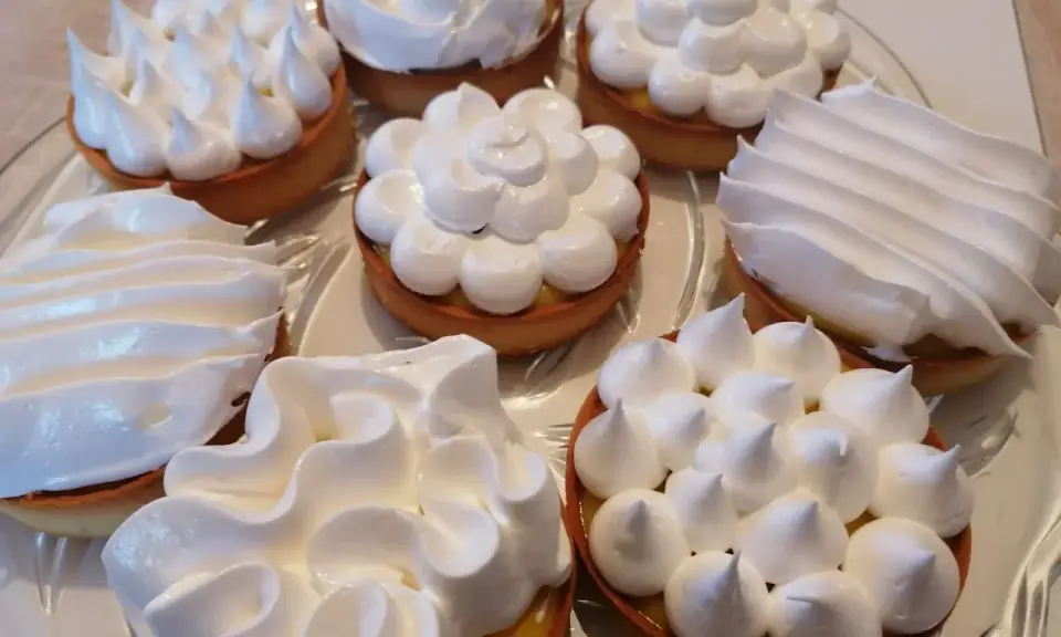 Plusieurs tartelettes garnies de crème citronnée et couronnées de meringue italienne aux formes variées.