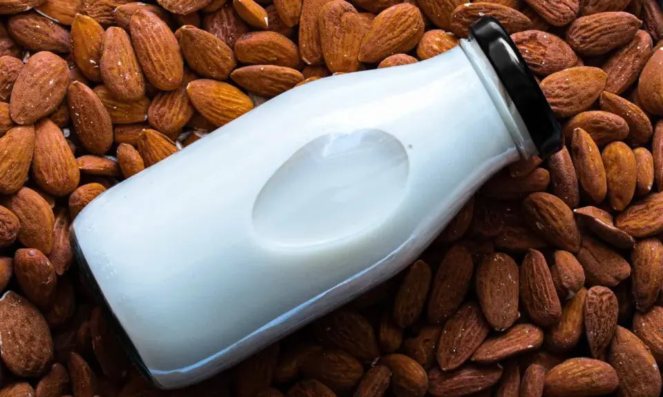 Bouteille de lait d'amande maison posée sur un lit d'amandes entières.