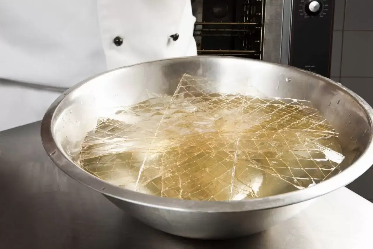 Feuilles de gélatine trempant dans un bol d'eau froide. C'est la première étape pour savoir comment utiliser la gélatine en feuille.