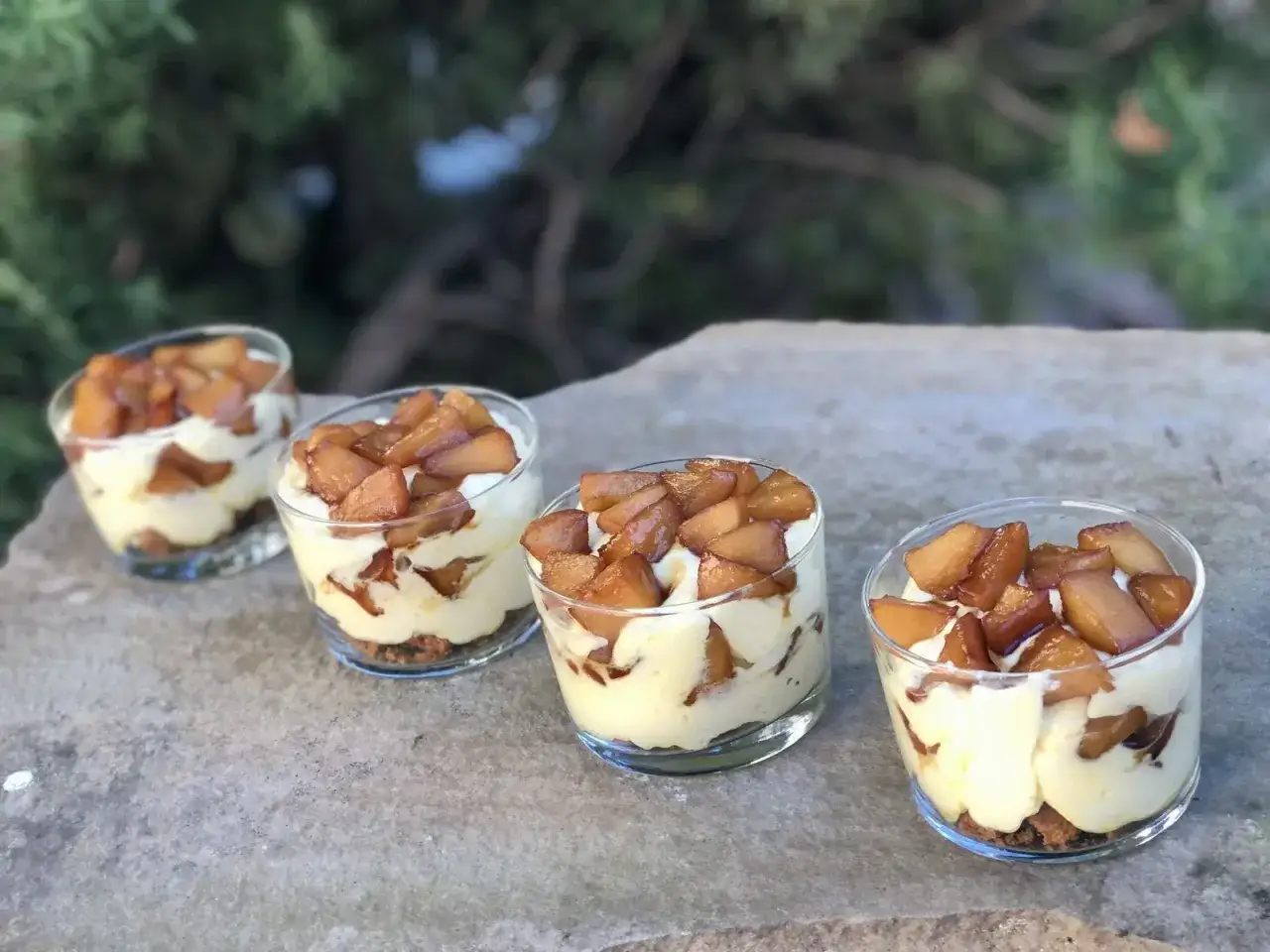 Quatre verrines de tiramisu pomme spéculoos, crémeux et gourmand, sur un fond de verdure.
