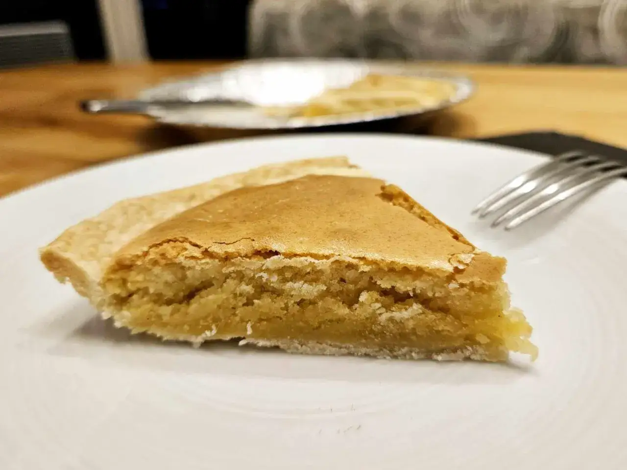 Tranche de tarte à la crème d'amandes légère, dorée et appétissante, sur une assiette blanche. Une fourchette est à côté.