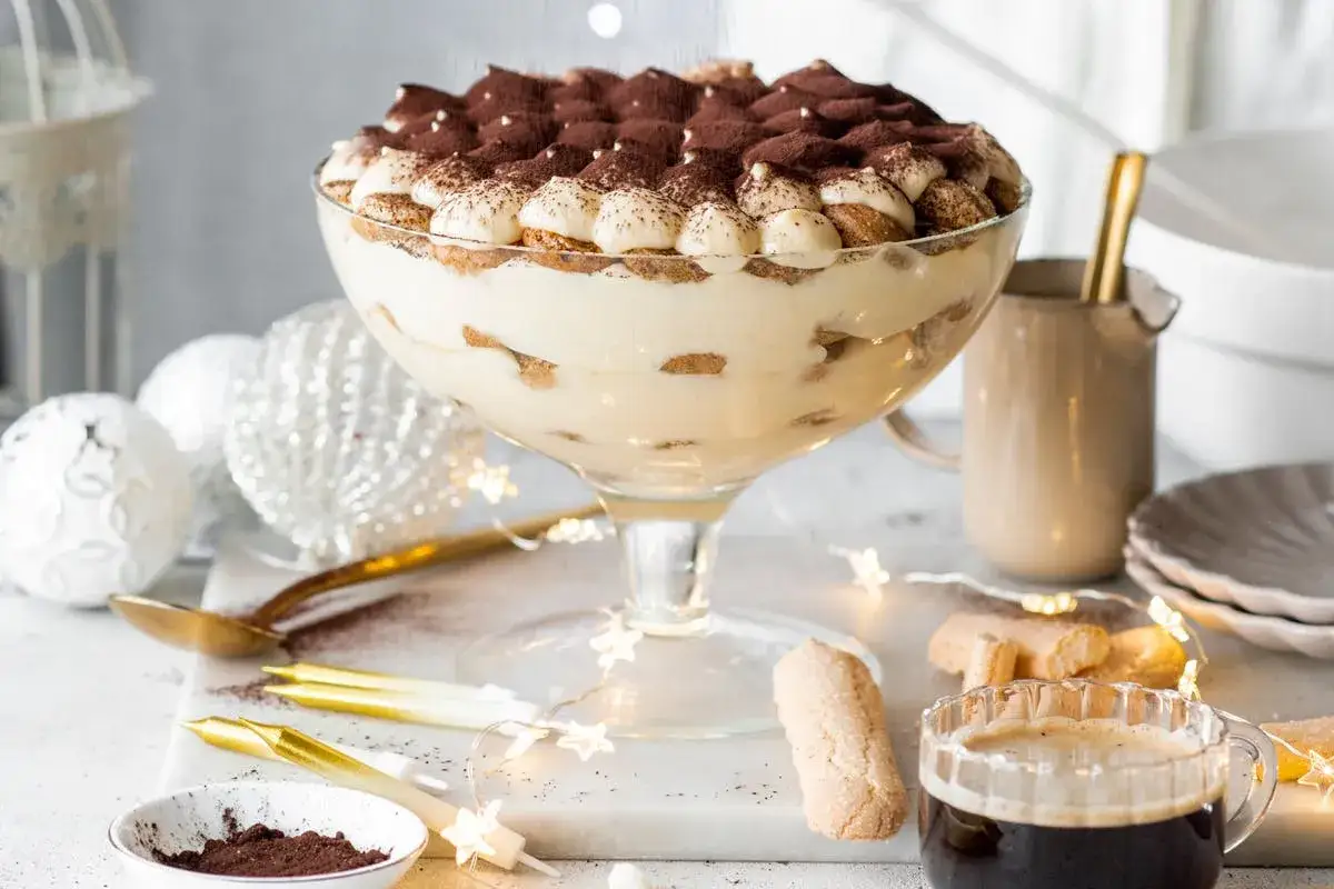 Un généreux tiramisu marsala, parsemé de cacao, dans un grand bol en verre, entouré de décorations festives et d'une tasse de café.