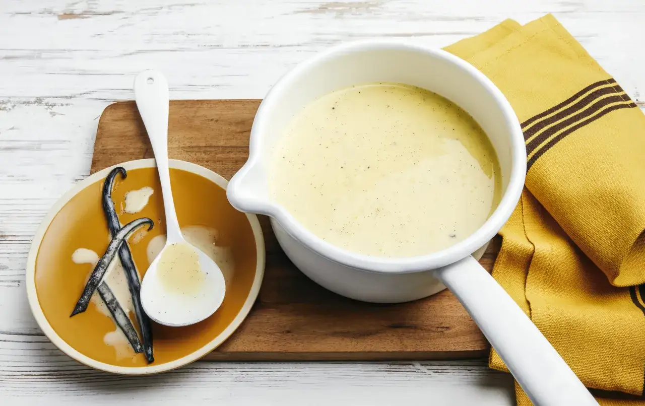 Crème anglaise onctueuse, prête à être dégustée. La recette crème anglaise grand-mère, avec des gousses de vanille sur une assiette.