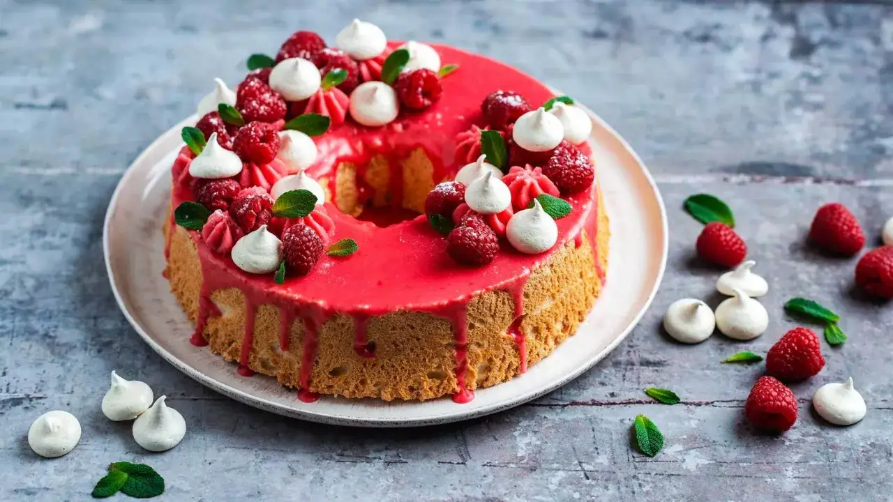 Un d&eacute;licieux angel cake rose vif, garni de framboises fra&icirc;ches, de meringues et de feuilles de menthe.