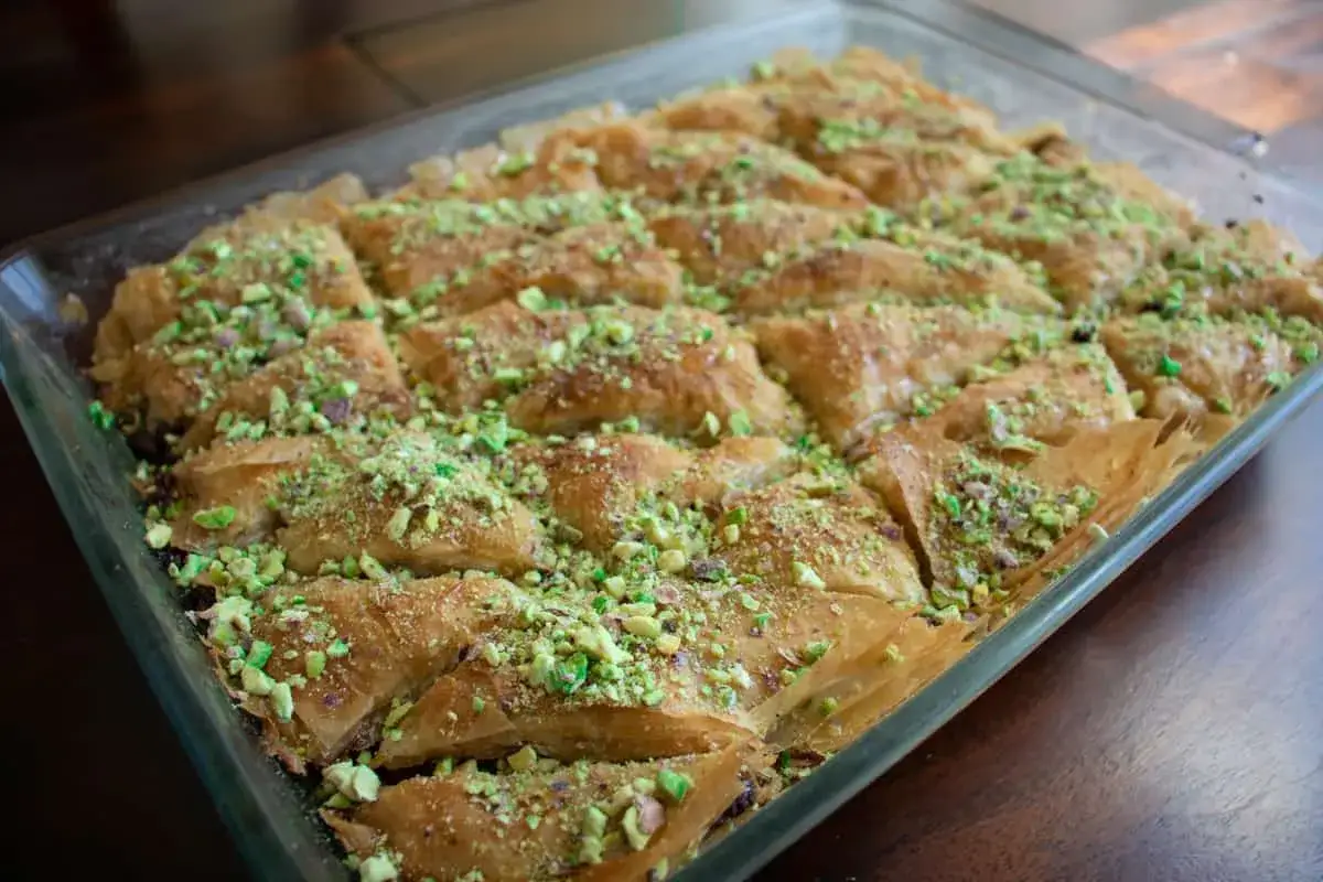Un plat de baklava maison, doré et croustillant, saupoudré de pistaches concassées. Une délicieuse recette de baklava à partager.